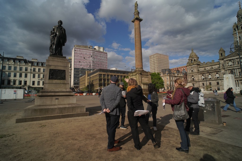 A group of people stand in front of a statue in George Square