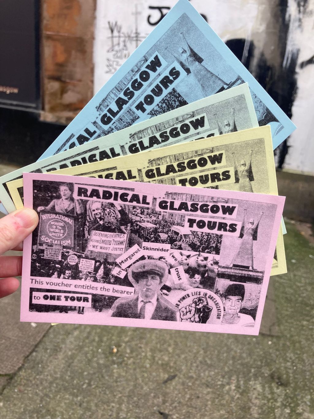 Hand fanning out four pastel coloured RGT tour vouchers, looking slightly like Monopoly money